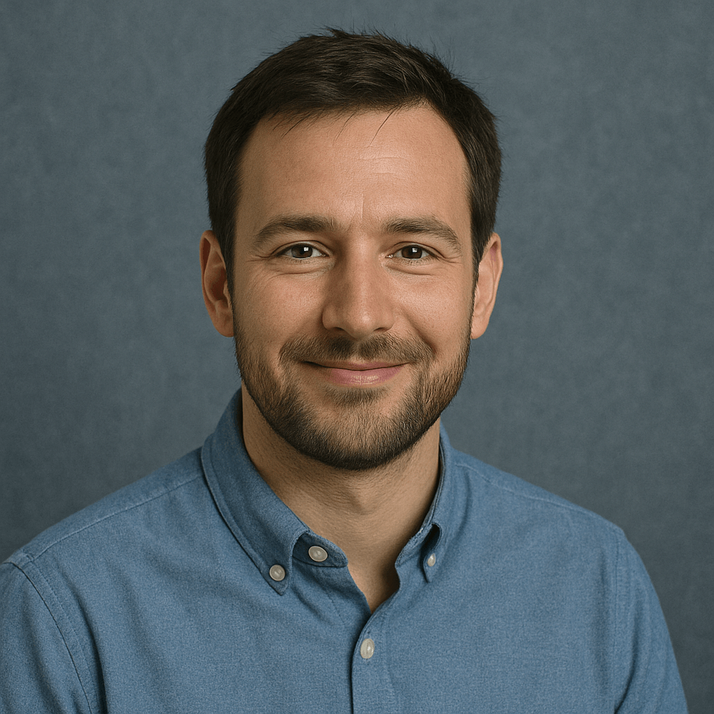 Porträt eines freundlich lächelnden Mannes mit dunklen Haaren und blauem Button-down-Hemd vor blau-grauem Hintergrund.