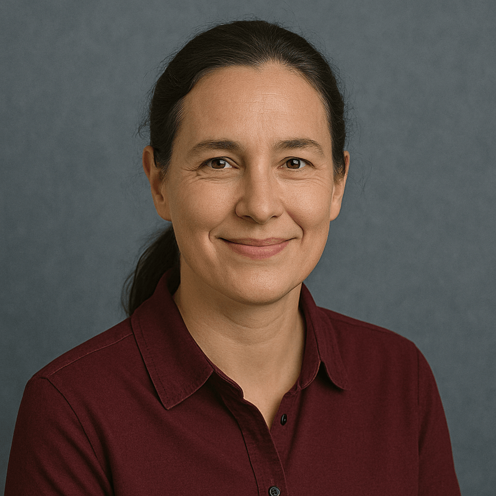 Porträt einer Frau mit dunkelbraunen Haaren im Zopf und burgunderrotem Hemd vor blau-grauem Hintergrund.